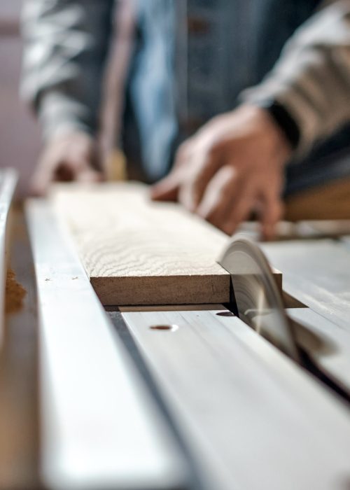 Caucasian man making wooden parts for custom furniture on machine tool called thickness planer in carpentry. Producing lumber concept